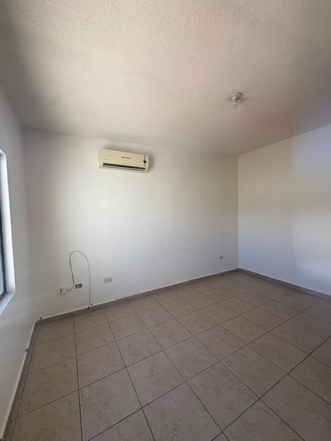 Recámara vacía con piso de loseta beige, paredes blancas, minisplit y ventana