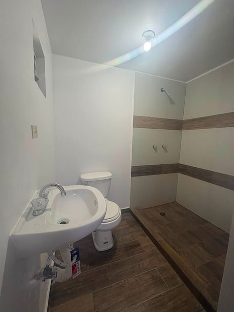 Baño moderno con lavamanos curvo blanco, inodoro, piso de madera y muros con acento de azulejo