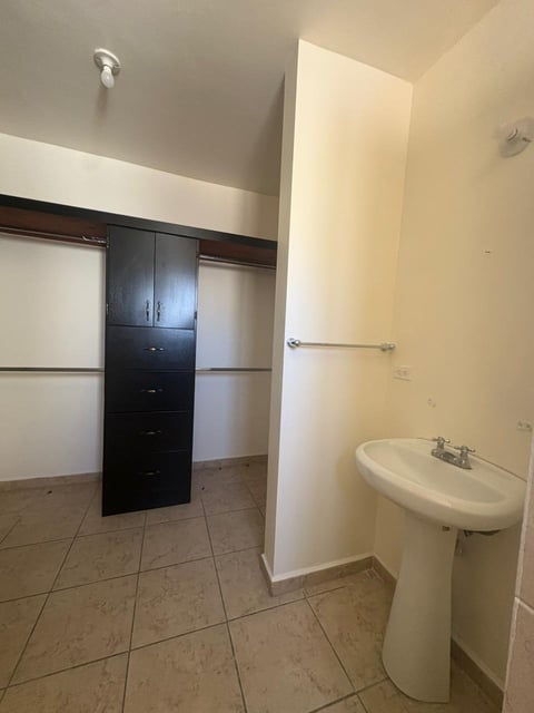 Walk-in closet y baño con paredes blancas, piso de loseta, lavamanos tipo pedestal y muebles de clóset negros