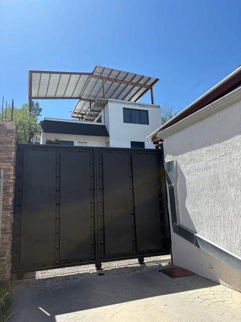 Fachada de casa moderna blanca con portón metálico negro y pérgola con paneles solares
