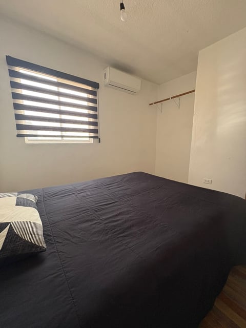 Recámara principal con cama, persianas azules, minisplit y piso de madera