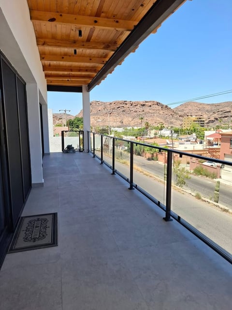 Patio cubierto moderno con techo de madera y barandilla de vidrio con vista al valle desértico y montañas