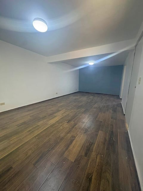 Recámara vacía con piso de madera oscura, paredes blancas, luminarias modernas y pared acento azul