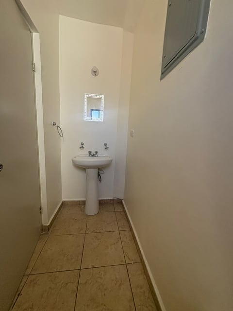 Baño angosto con lavamanos tipo pedestal, piso de loseta y ventana pequeña sobre el lavabo