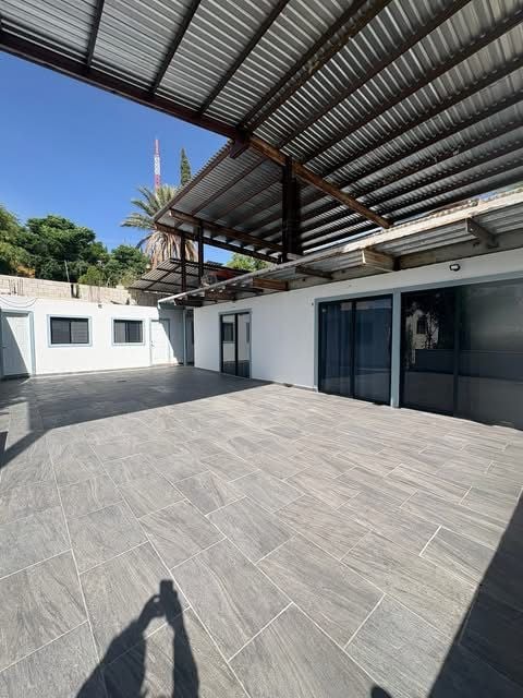 Terraza con piso de loseta gris, pérgola metálica y palmera