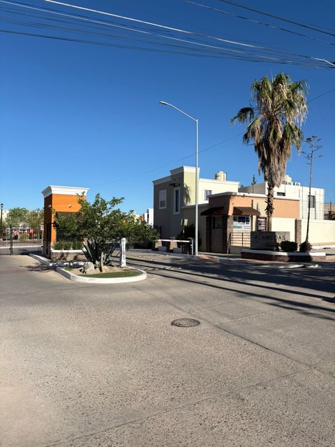Vista de la calle de la privada con casas modernas color naranja y crema, palmeras y acceso controlado