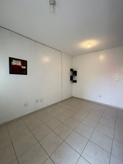 Sala vacía con piso de loseta claro, paredes blancas, focos de techo y cuadro abstracto en pared