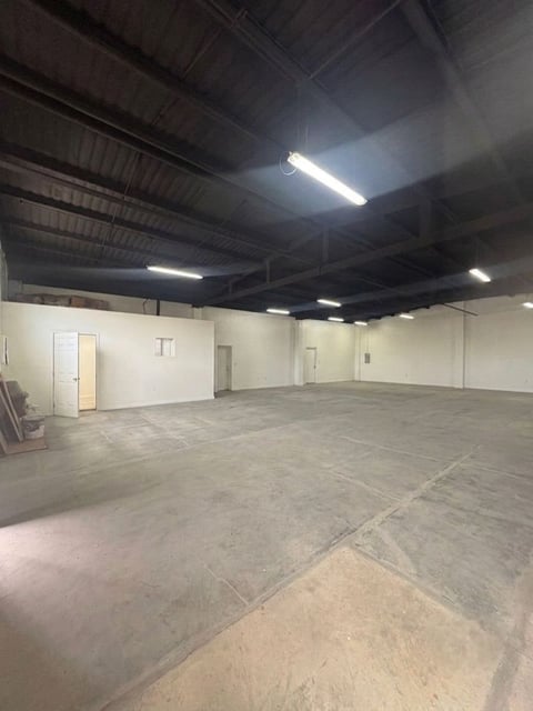 Bodega o almacén industrial con piso de concreto, vigas expuestas en techo, lámparas fluorescentes y puertas de oficina blancas
