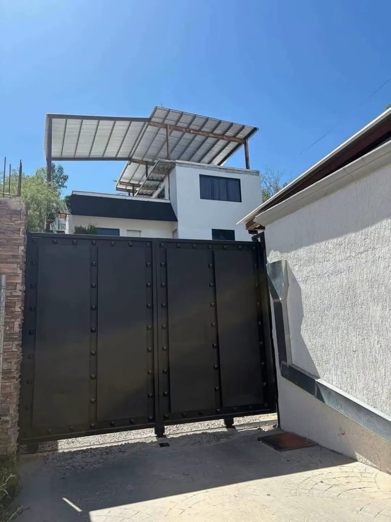 Modern white house with solar panel pergola roof visible above black metal entry gate and driveway