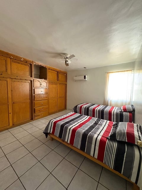 Recámara con dos camas, ropa de cama color rojo y negro, clósets de madera y ventilador de techo