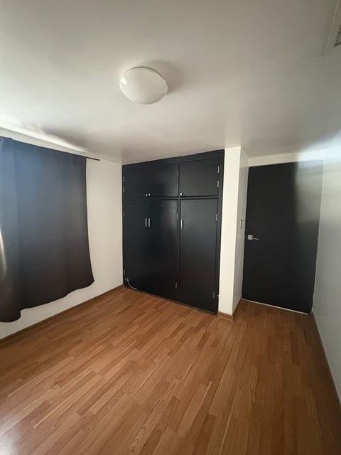 Habitación con piso de madera, muros blancos y puertas de clóset negras