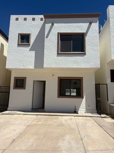 Fachada de casa blanca de dos pisos con ventanas de marco oscuro y portón metálico