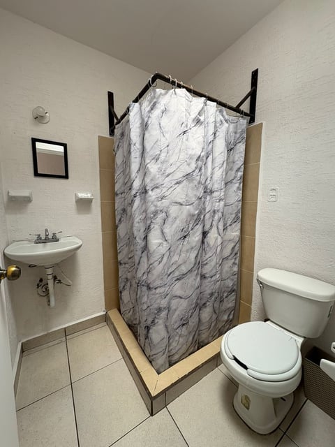 Baño completo con lavamanos blanco, inodoro y regadera con cortina tipo mármol
