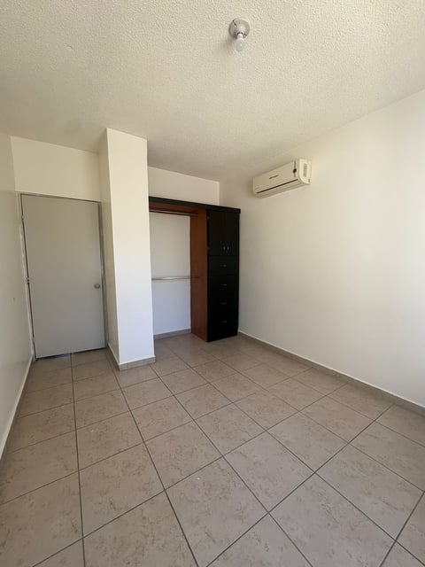 Interior vacío con paredes beige, piso de loseta, muro divisorio blanco, puerta abierta y minisplit en pared