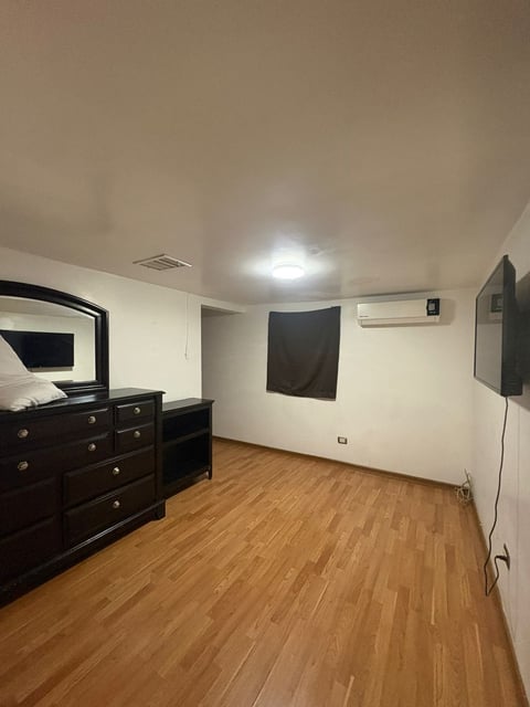 Recámara con vestidor de madera oscura, espejo, piso laminado y TV en la pared