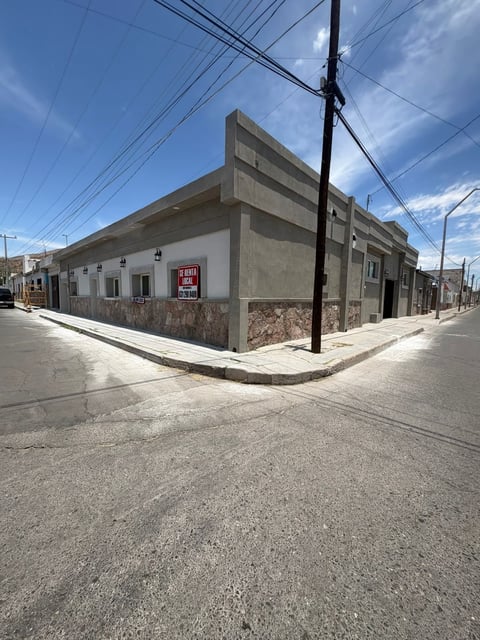 Esquina de edificio comercial abandonado con fachada de concreto desgastado y letrero rojo de Se Vende en calle residencial soleada