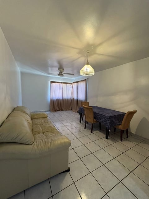 Sala-comedor amplia con sofá beige, mesa de comedor con sillas café y lámpara colgante