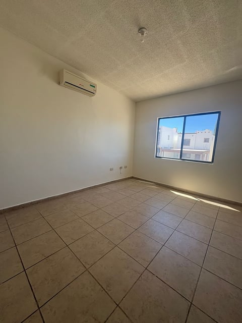 Recámara vacía con paredes beige, piso de loseta, ventana con vista a la ciudad y minisplit