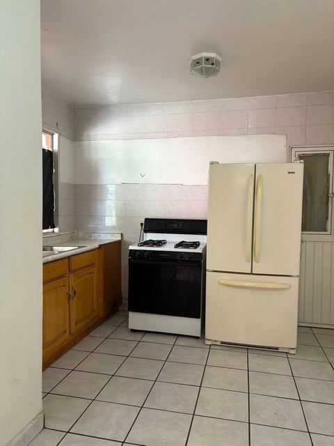 Cocina con gabinetes de madera, estufa negra y refrigerador color crema