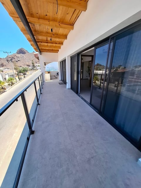 Balcón amplio con techo de madera, puertas corredizas de vidrio oscuro y barandilla metálica con vista a las montañas costeras