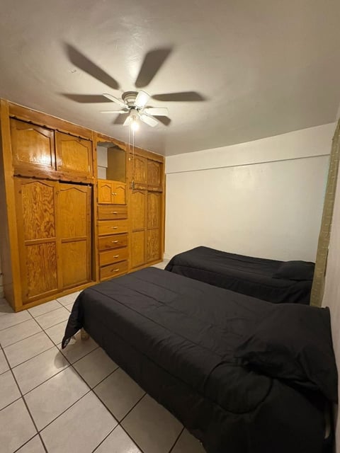 Recámara con dos camas individuales, edredones negros, clóset de madera y ventilador de techo