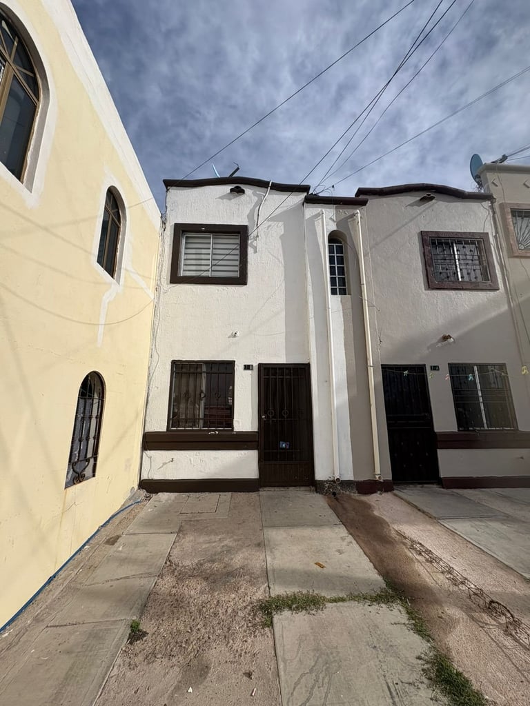 Row of narrow residential townhouses with white and cream facades, dark brown doors and windows, and power lines overhead on a sunny day