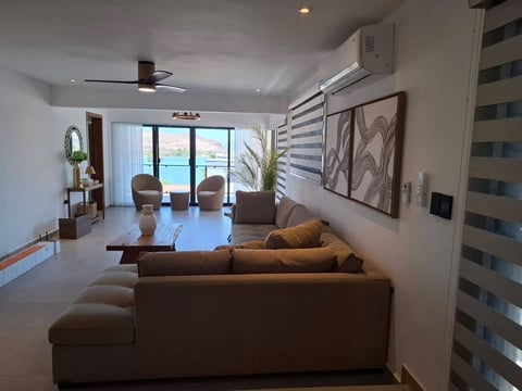 Sala moderna de apartamento de gran altura con sofá seccional café, vista al mar, abanico de techo y arte contemporáneo