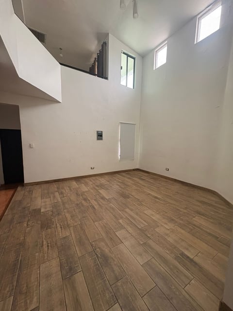 Espacio tipo loft con techos altos, piso de madera y entrepiso con ventanas