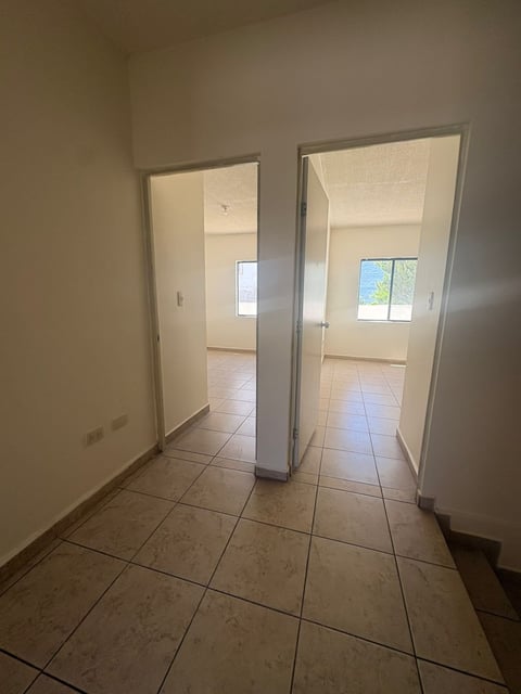 Pasillo interior con piso de loseta y dos puertas abiertas hacia recámaras iluminadas con ventanas