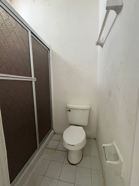 Baño con regadera de puerta de vidrio, inodoro y piso de loseta blanca