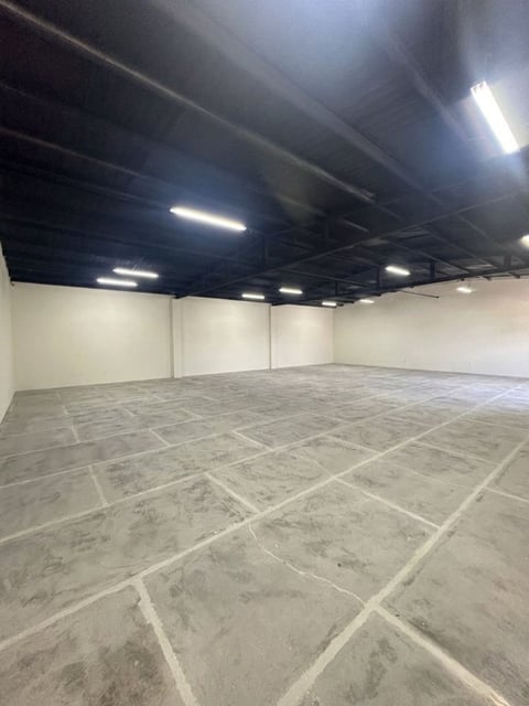 Bodega vacía con piso de concreto, muros blancos, techo negro con luces LED y rejilla de ventilación