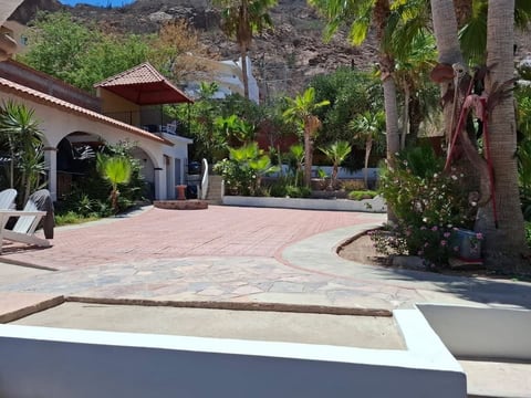 Propiedad desértica con patio de ladrillo, cochera, palmeras y cerro al fondo bajo cielo azul