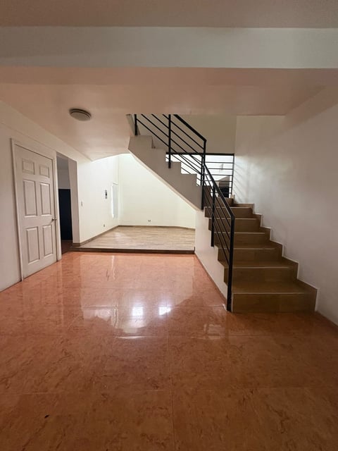 Vestíbulo interior con piso, muros blancos y escalera con barandal metálico