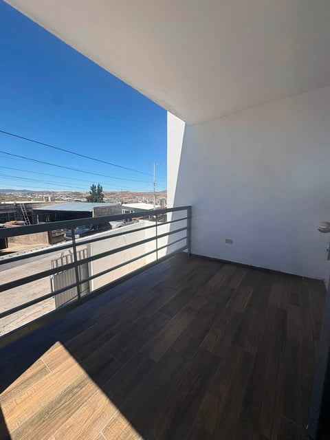 Balcón moderno con piso de madera oscura y barandilla metálica con vista panorámica a la ciudad bajo cielo azul