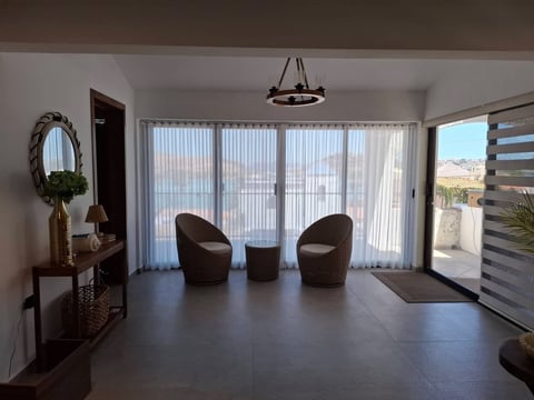 Sala moderna con dos sillones de mimbre, mesa central, cortinas sheer, consola de madera y vista al paisaje desértico