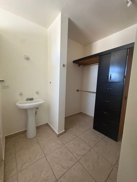 Baño y clóset con lavamanos tipo pedestal, puertas de clóset color negro y piso de loseta