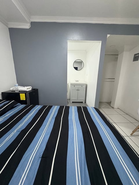 Recámara moderna con ropa de cama rayada azul y negra, pared acento gris y baño visible