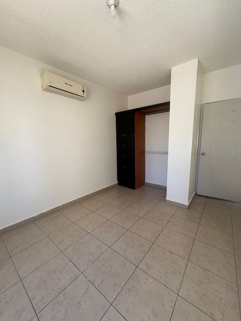 Recámara vacía con piso de loseta beige, paredes blancas, minisplit en pared y clóset de madera oscura