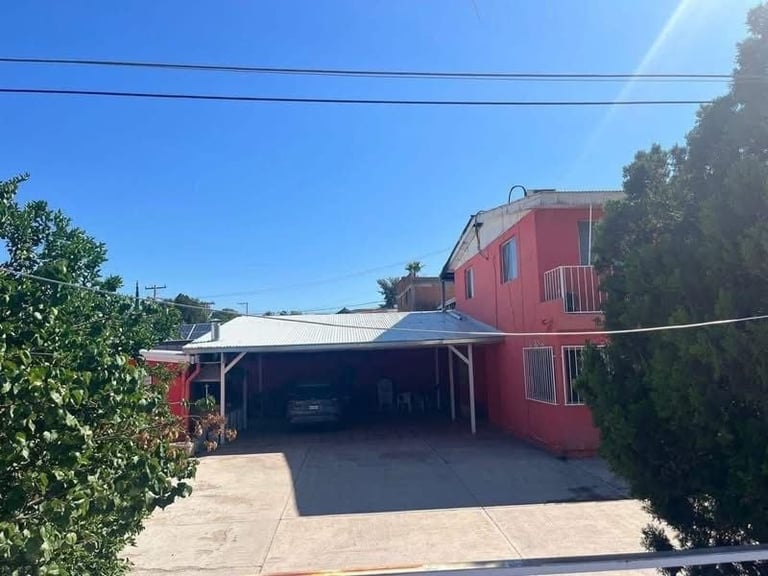 Red residential house with attached carport and surrounding greenery on a sunny day