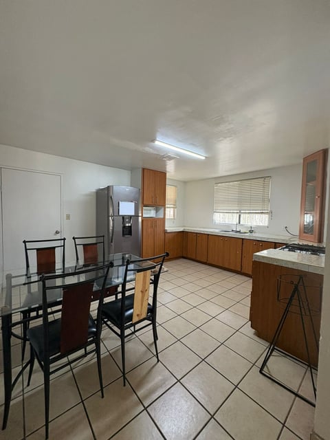 Cocina con mesa de comedor, gabinetes de madera y refrigerador de acero inoxidable
