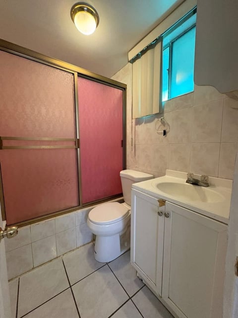 Baño con muros de loseta blanca, lavamanos e inodoro