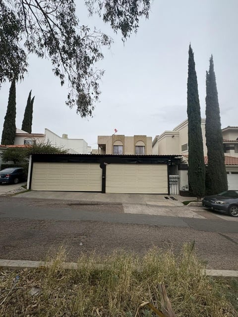 Casa residencial moderna con cochera doble, cipreses altos y camino de piedra en zona suburbana