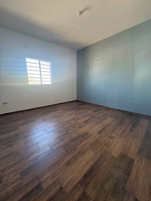 Recámara con piso de madera, paredes azul claro, techo blanco y ventana con persianas