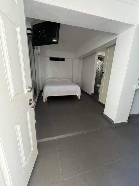 Recámara minimalista con cama individual, paredes blancas y TV en la pared