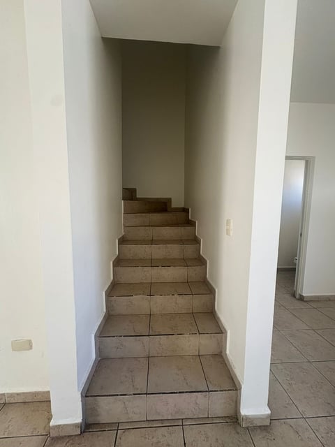 Escalera interior con escalones de loseta beige, paredes blancas e iluminación neutra