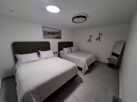 Recámara estilo hotel con dos camas, cabeceras oscuras, ropa de cama blanca, arte playero de costa y decorado contemporáneo