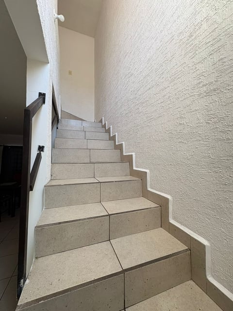 Escalera interior con escalones de piedra clara, muros blancos y barandal metálico