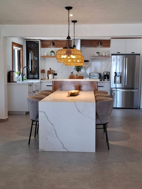 Cocina moderna con gabinetes blancos, isla con cubierta de mármol, lámparas tejidas colgantes y electrodomésticos de acero inoxidable