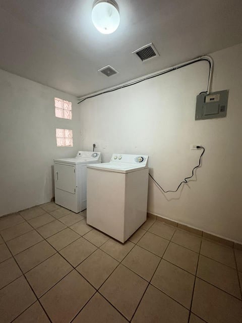 Cuarto de lavado con lavadora y secadora blancas sobre piso de loseta, ventilación de techo, contacto y tendedero