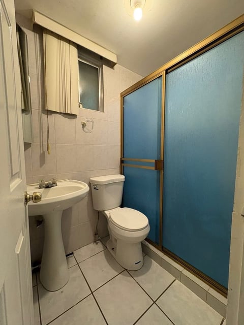 Baño con lavamanos de pedestal blanco, regadera de vidrio azul e inodoro